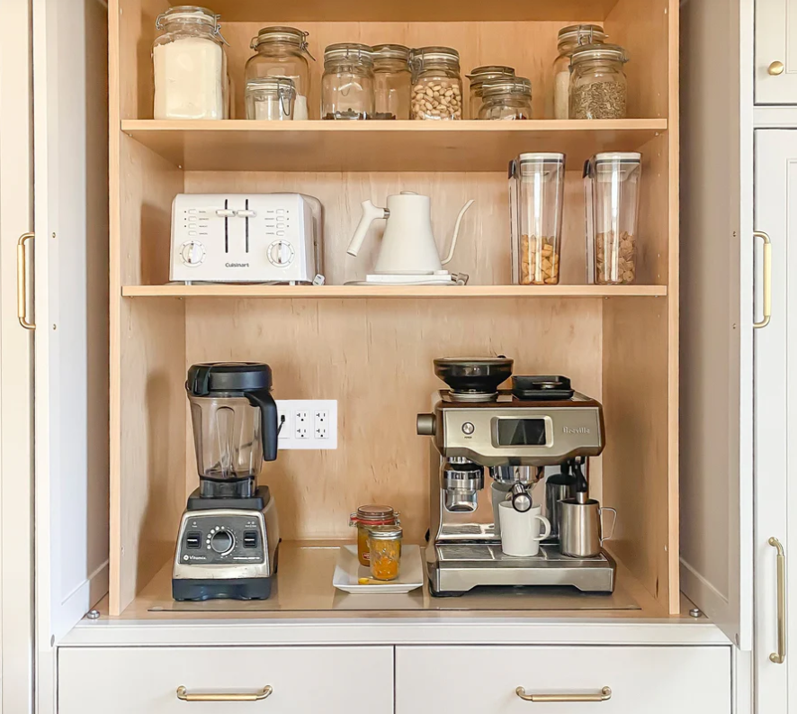 Open cabinet with a blender on the lower left a coffee espresso machine on the lower right a toaster and kettle on the middle shelf and jars on the top shelf