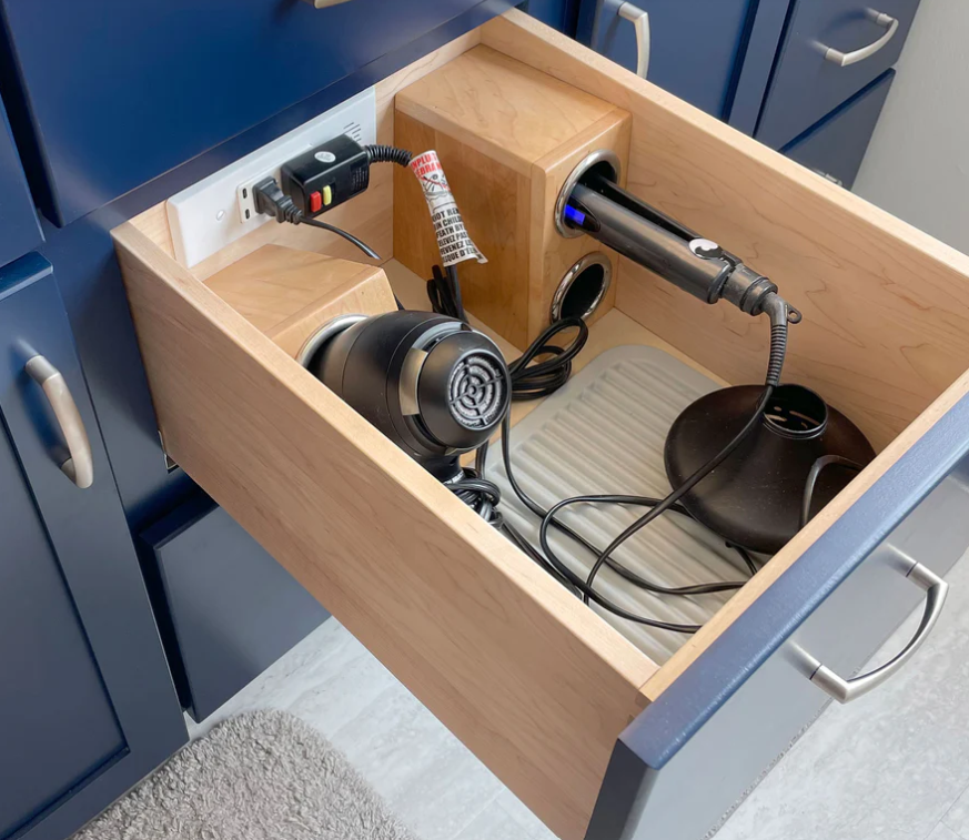 Drawer with hair styling tools hair dryer curling wand heat diffuser and tangled cords visible inside a wooden drawer
